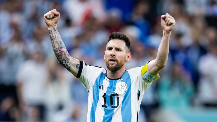 Lionel Messi steht im Trikot von Argentinien mit der Nr. 10 vor der Kurve und reckt beide Fäuste in die Höhe.