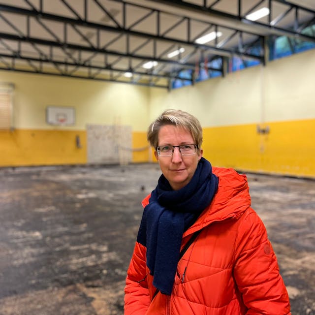 Jana Herrmann, Vertreterin der Schulpflegschaft der KGS Kupfergasse in Urbach, steht in der maroden Turnhalle der Schule. Der Bode ist schwarz, hinter ihr ist ein Gerüst für die Arbeiten aufgebaut.