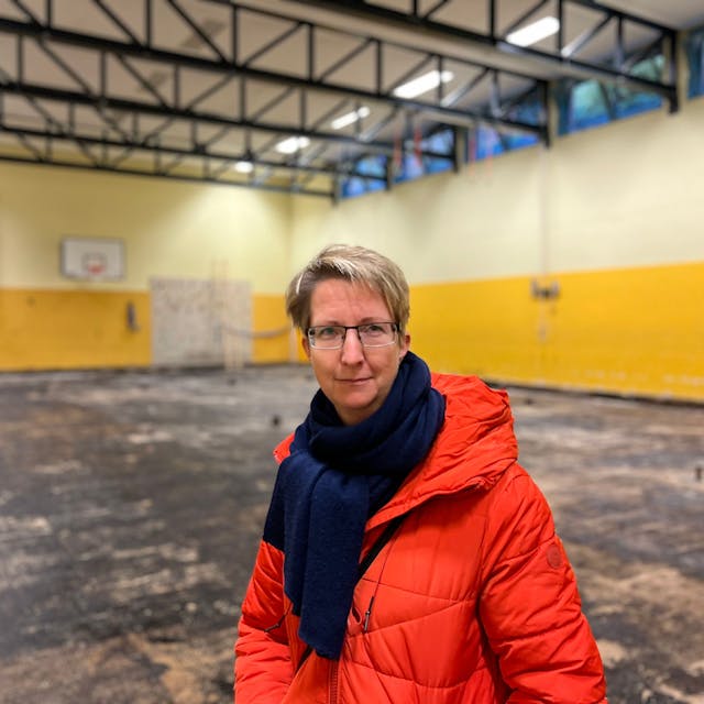 Jana Herrmann, Vertreterin der Schulpflegschaft der KGS Kupfergasse in Urbach, steht in der maroden Turnhalle der Schule. Der Bode ist schwarz, hinter ihr ist ein Gerüst für die Arbeiten aufgebaut.