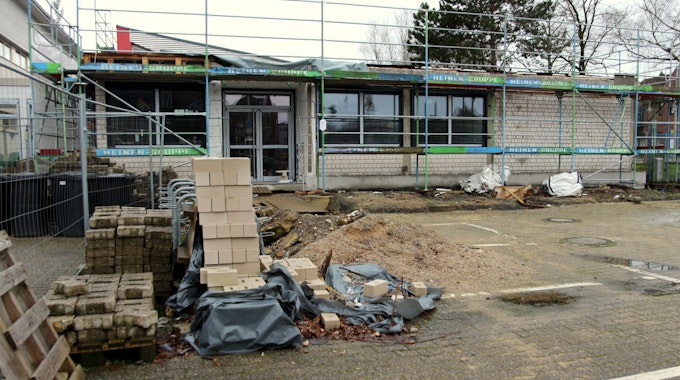 Auf dem Foto ist ein Erweiterungsbau der Horionschule in Pulheim zu sehen. Das Gebäude ist eingerüstet, davor liegt Baumaterial wie Steine und Sand.