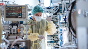 Ein Mitarbeiter in Schutzkleidung steht zwischen vielen medizinischen Geräten und Kabeln.