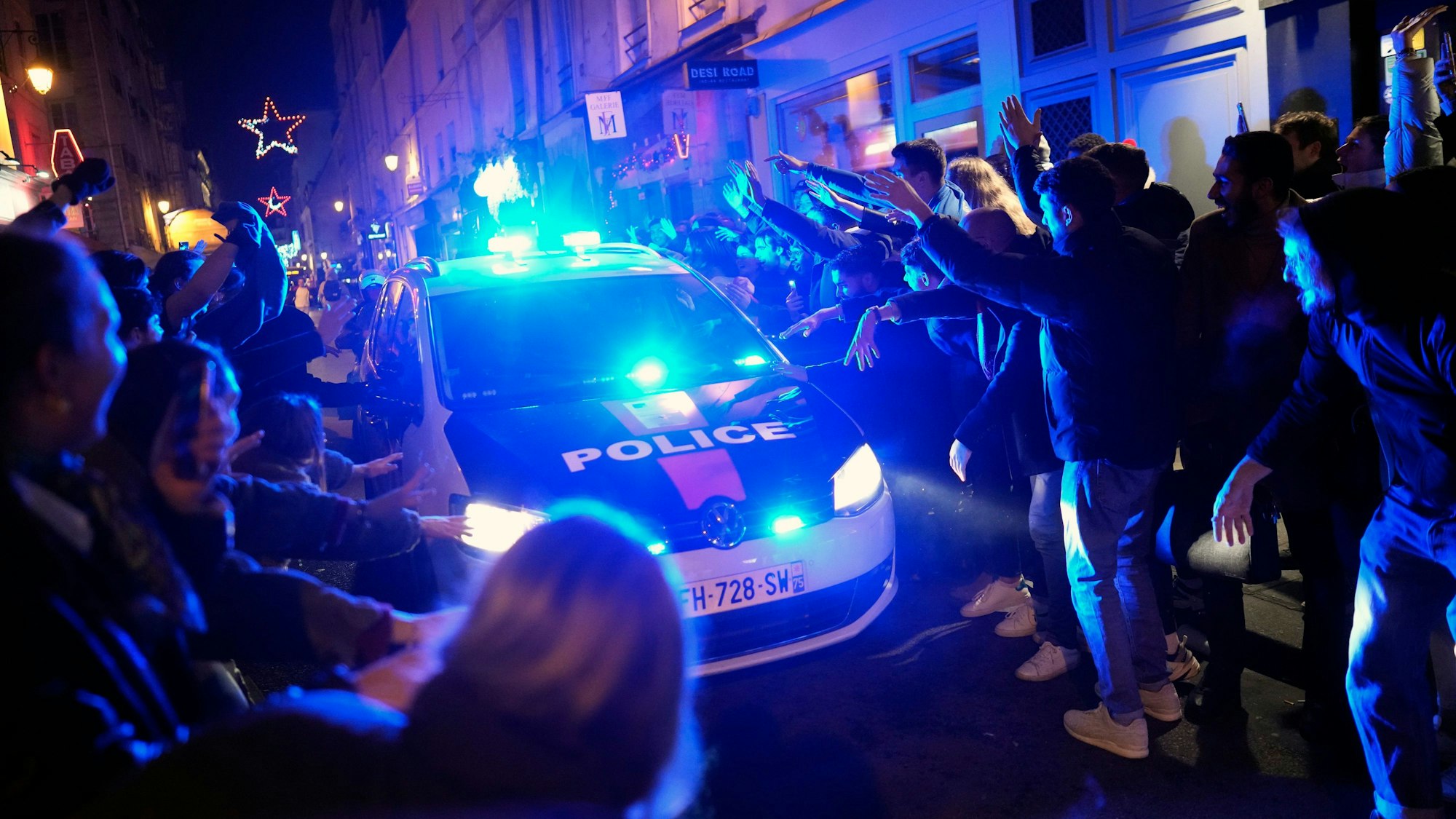 Französische Fans stehen in Paris nach dem WM-Halbfinale neben einem Polizeiauto mit Blaulicht.