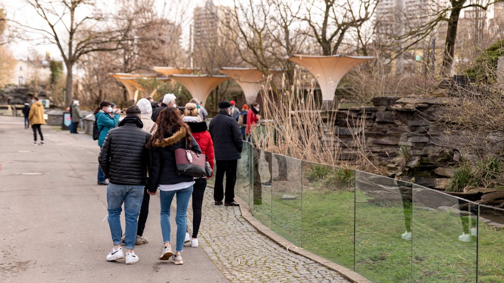 Menschen gehen in dicken Klamotten durch den Kölner Zoo. Rechts ist ein kleineres Gehege zu sehen.