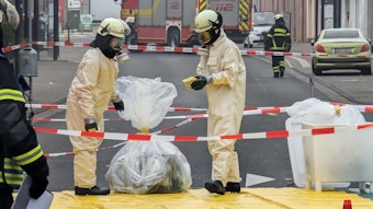 Feuerwehrleute in Sicherheitsanzügen und mit Atemschutzmasken sichern in Plastiksäcken Material aus der Arztpraxis.