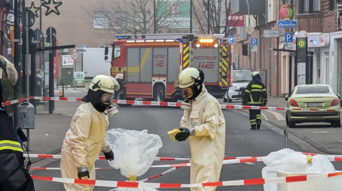 Feuerwehrleute in Sicherheitsanzügen und mit Atemschutzmasken sichern in Plastiksäcken Material aus der Arztpraxis.