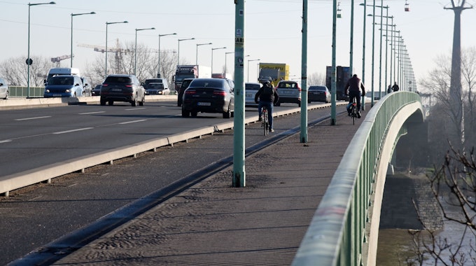Viel Verkehr auf der Kölner Zoobrücke. Neben Autos und Lkws fahren Radfahrer. Viele Laternenmasten stehen am Straßenrand.