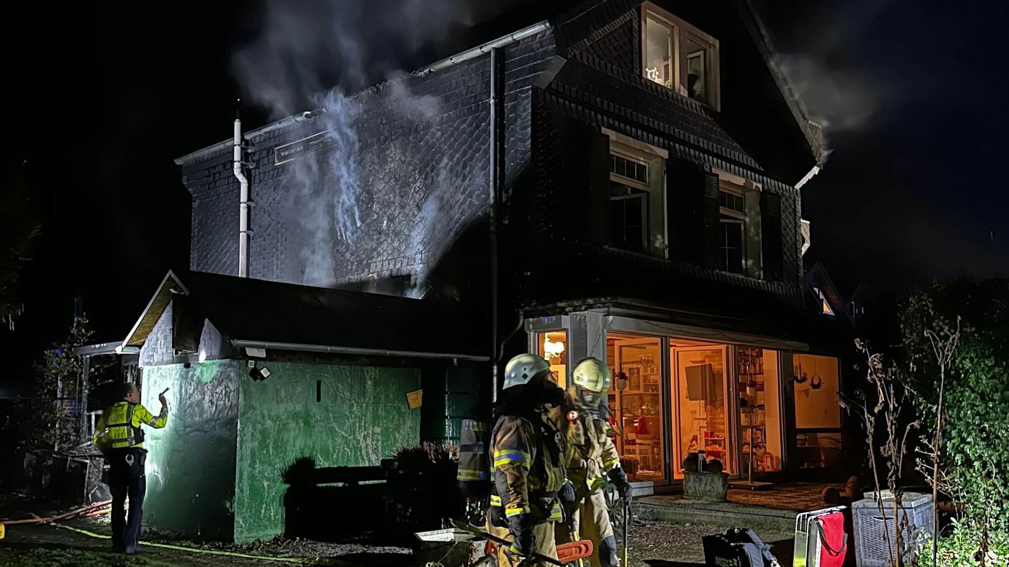 Feuerwehrleute und Polizei an dem noch rauchenden Brandhaus in Bergisch Gladbach-Schildgen.