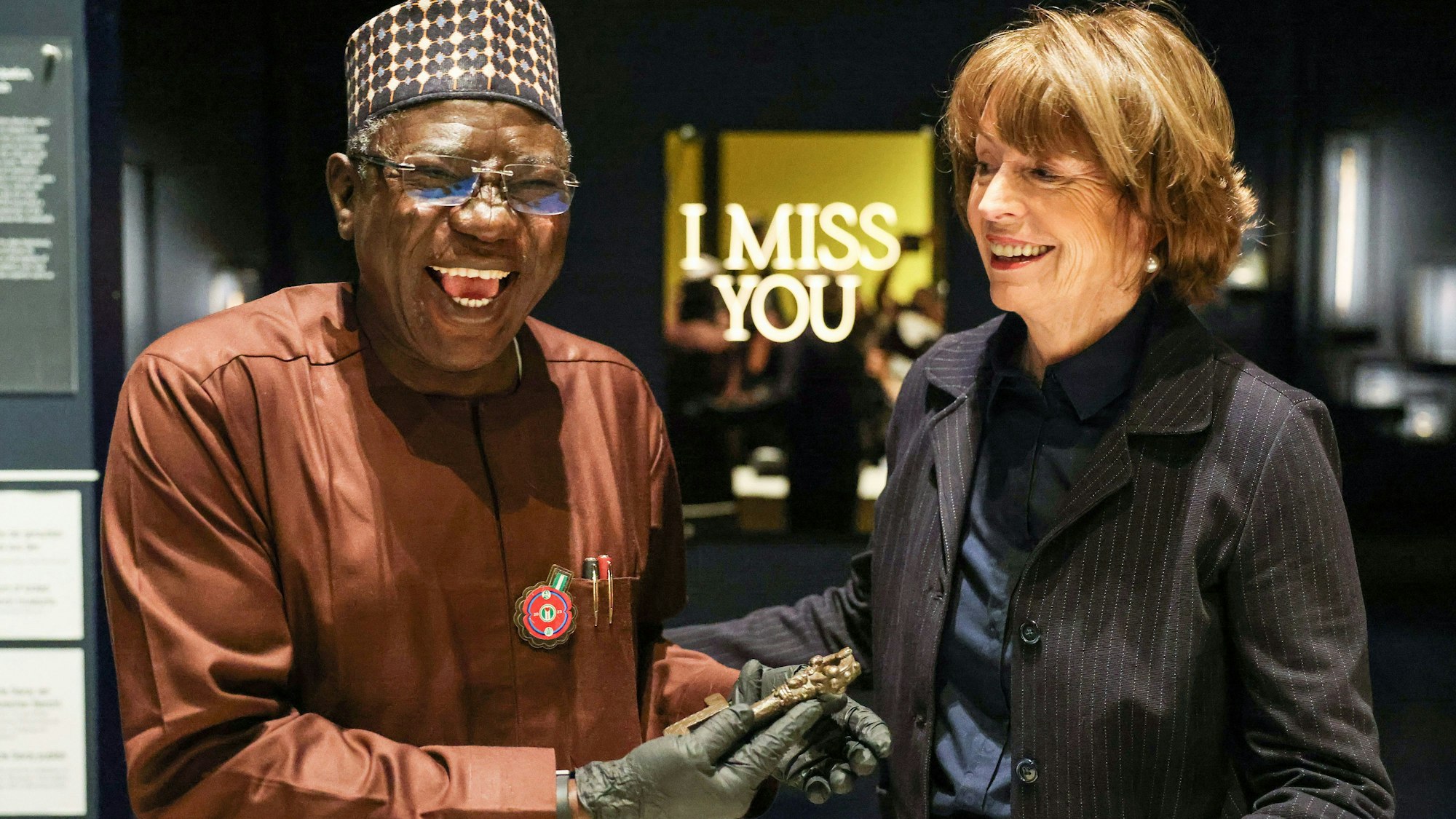 Henriette Reker, Oberbürgermeisterin von Köln, übergibt einem freudig lachenden Abba Isa Tijani, Generaldirektor der Nationalen Kommission für Museen und Monumente, symbolisch einen bronzenen Schlüssel aus dem Königreich Benin.