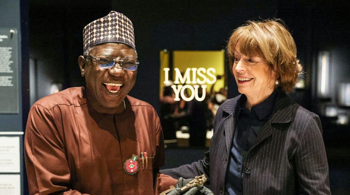 Henriette Reker, Oberbürgermeisterin von Köln, übergibt einem freudig lachenden Abba Isa Tijani, Generaldirektor der Nationalen Kommission für Museen und Monumente, symbolisch einen bronzenen Schlüssel aus dem Königreich Benin.