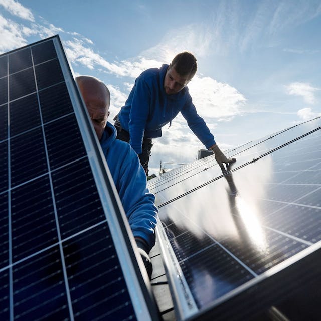 Techniker montieren Photovoltaikmodule auf dem Dach eines Wohnhauses.
