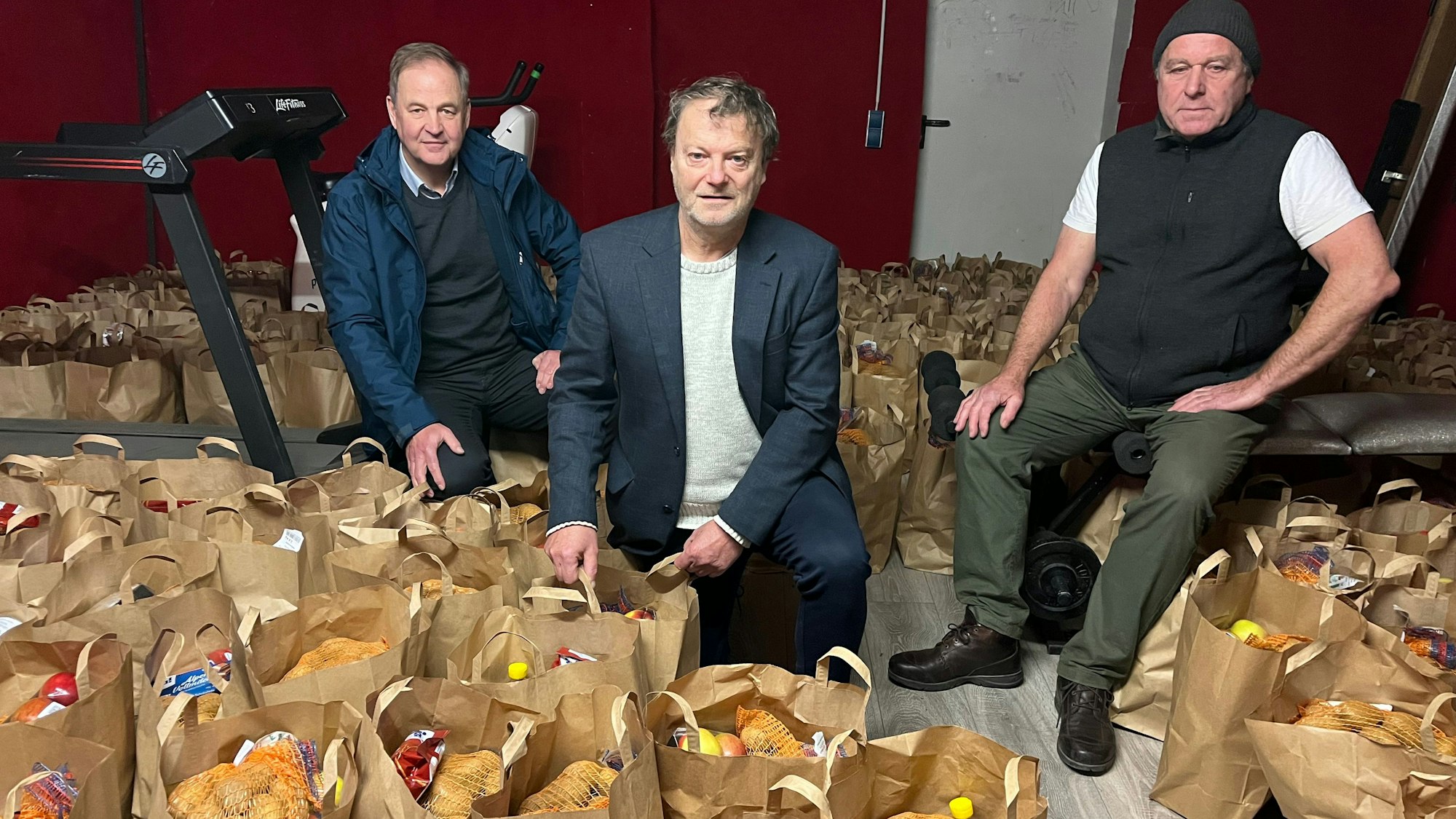 Drei Männer stehen inmitten von Tüten mit Lebensmittelspenden