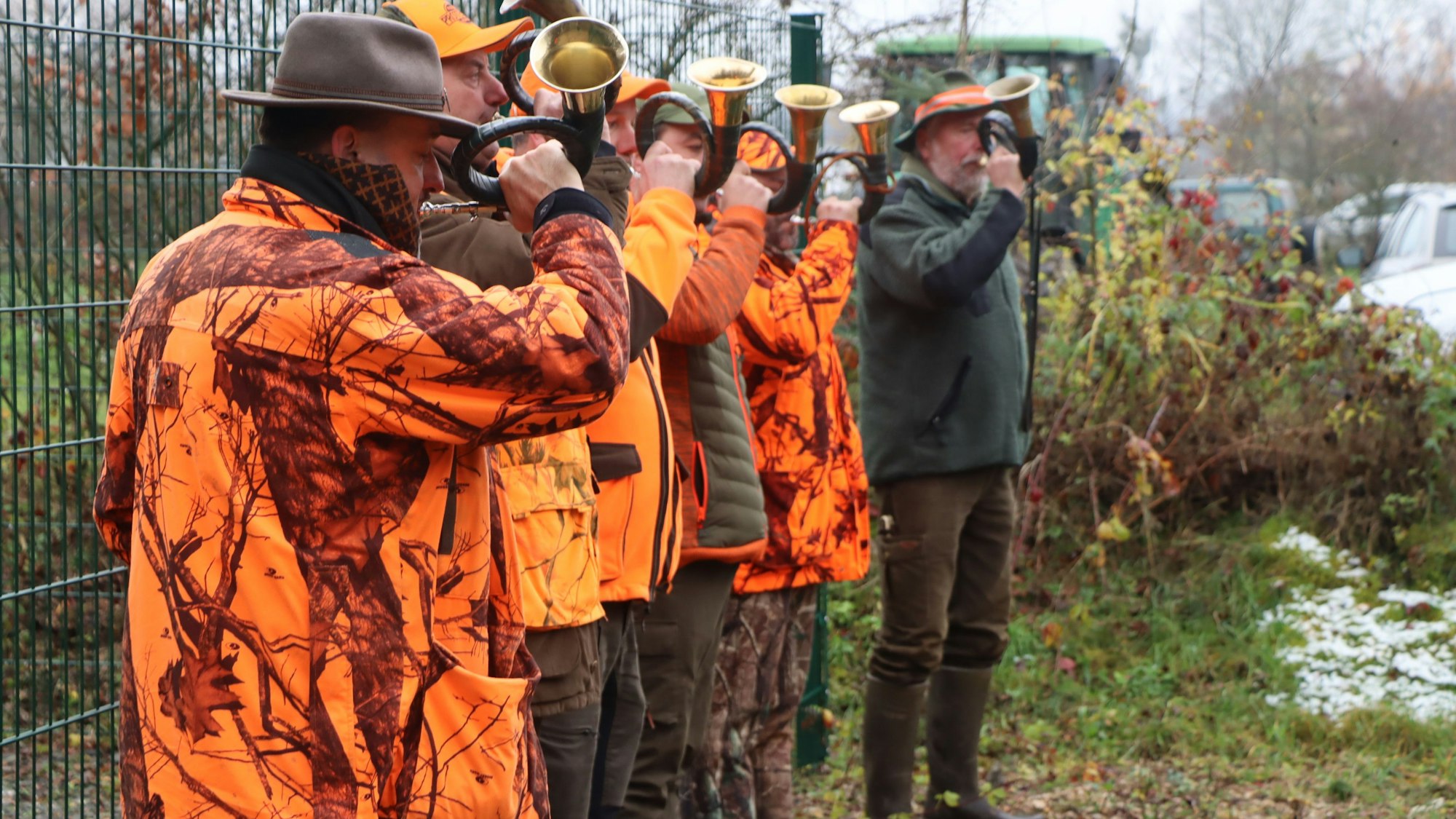 Jäger in orangefarbenen Jacken blasen in ihre Jagdhörner.