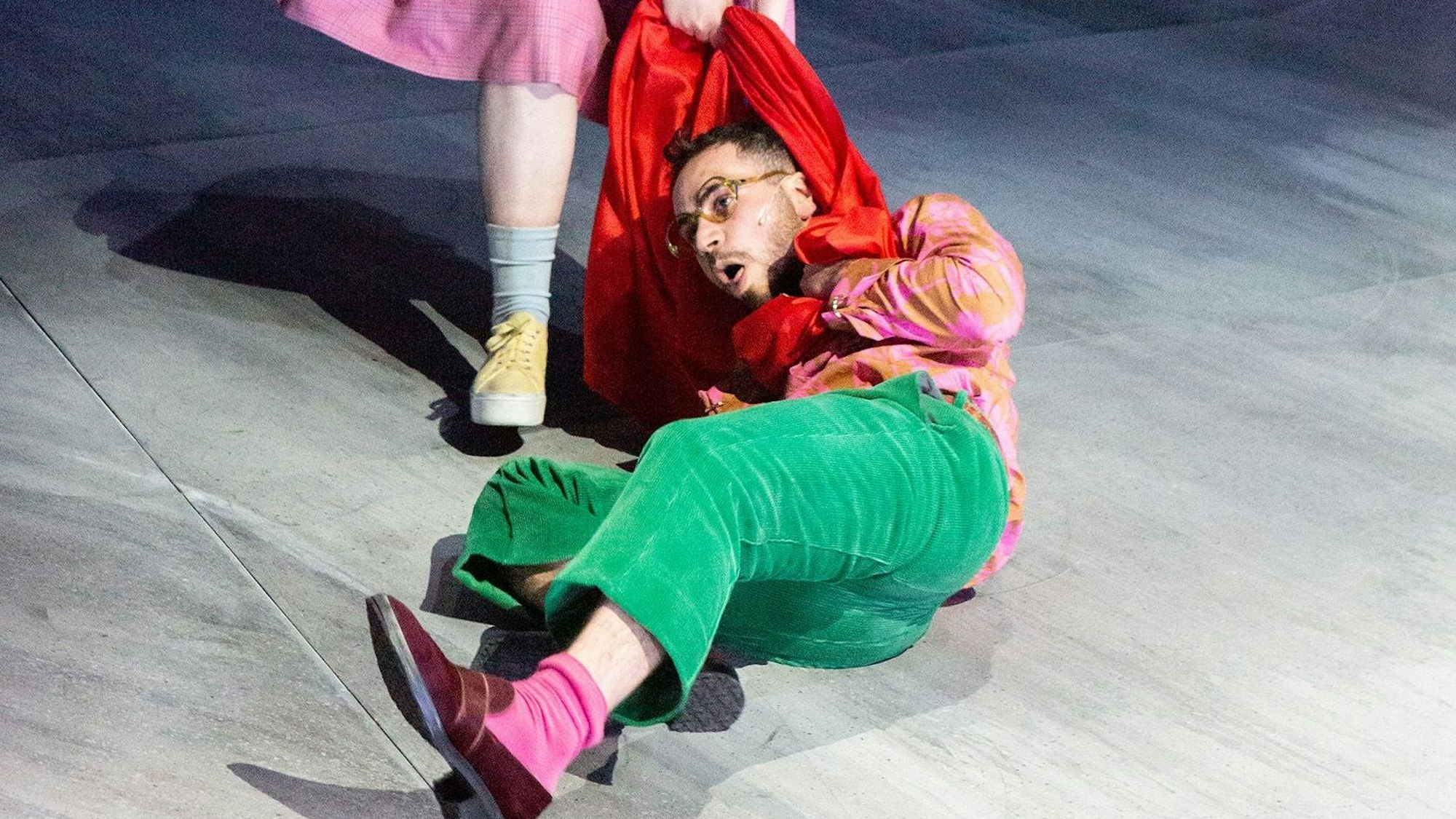 Szene Helges Leben am Schauspiel Köln, ein Mann am Boden wird an seinem roten Schal über die Bühne gezerrt.