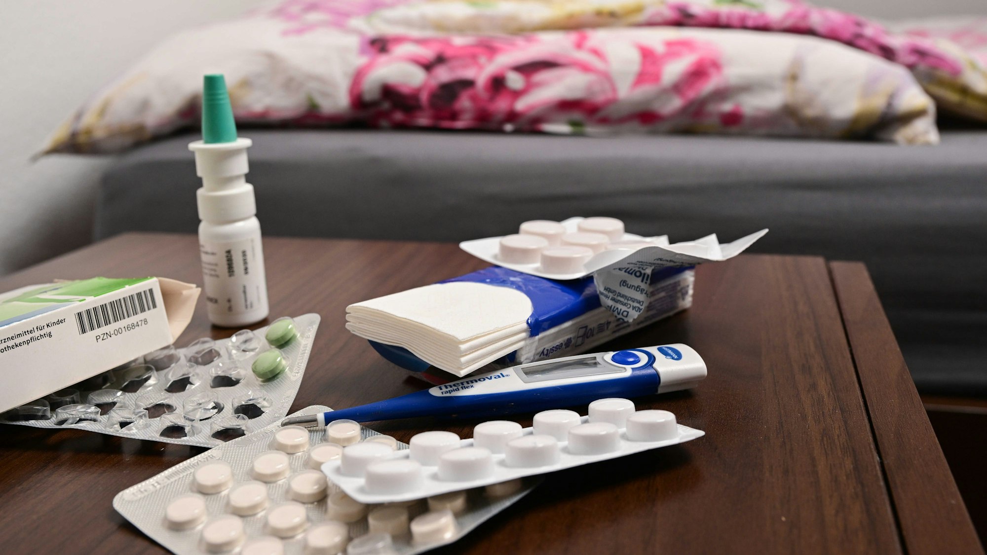 Ein Fieberthermometer und Medikamente liegen auf einem Nachttisch (gestellte Szene).