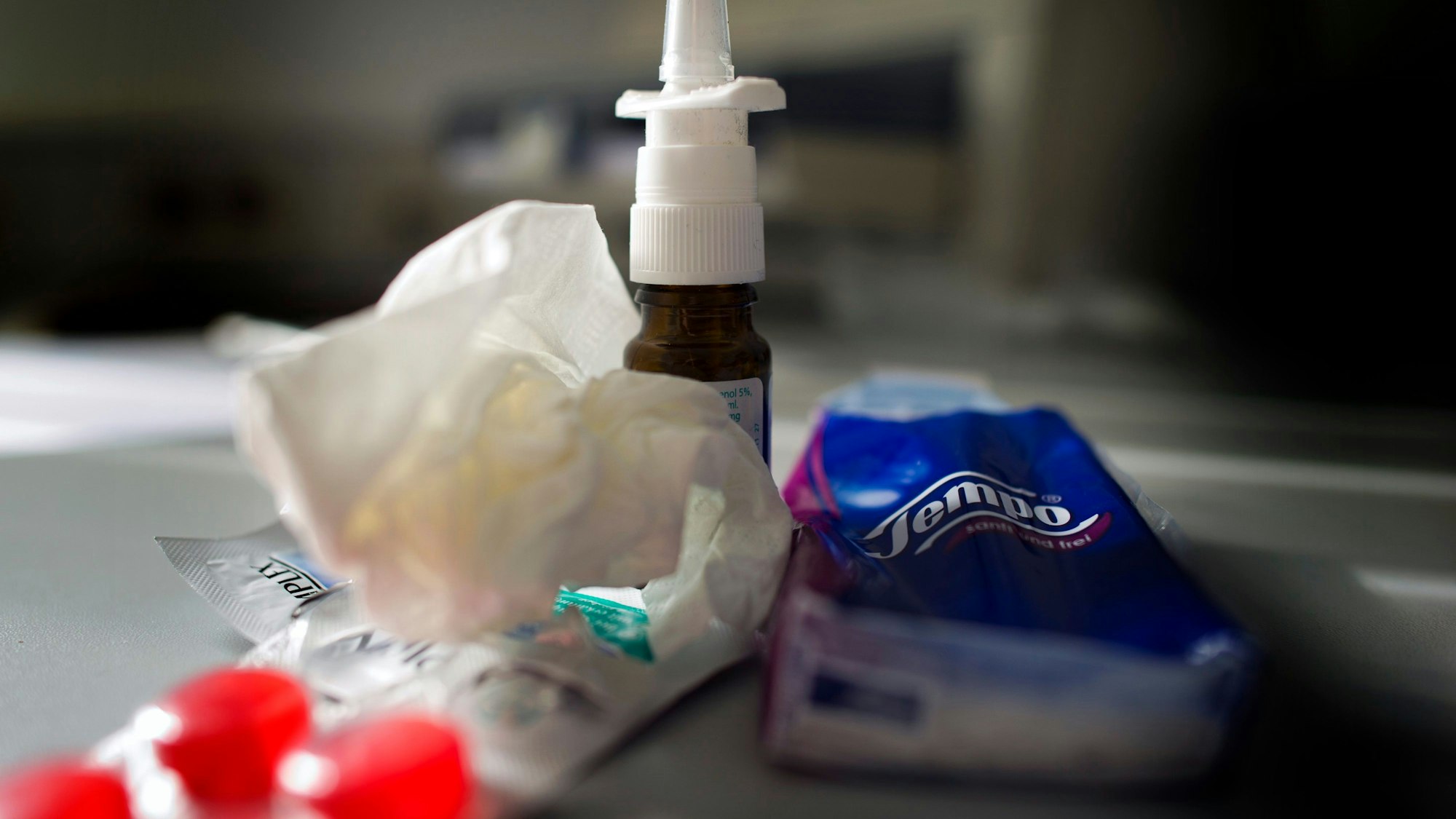 Anti-Erkältungsmittel wie Nasenspray, Halstabletten und Papiertaschentücher liegen auf einem Tisch.