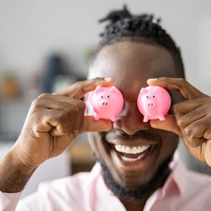 Mann hält sich zwei rosa mini-Sparschweinchen vor die Augen.