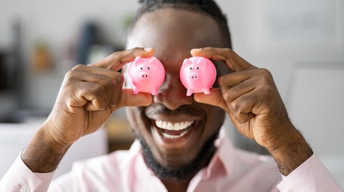 Mann hält sich zwei rosa mini-Sparschweinchen vor die Augen.