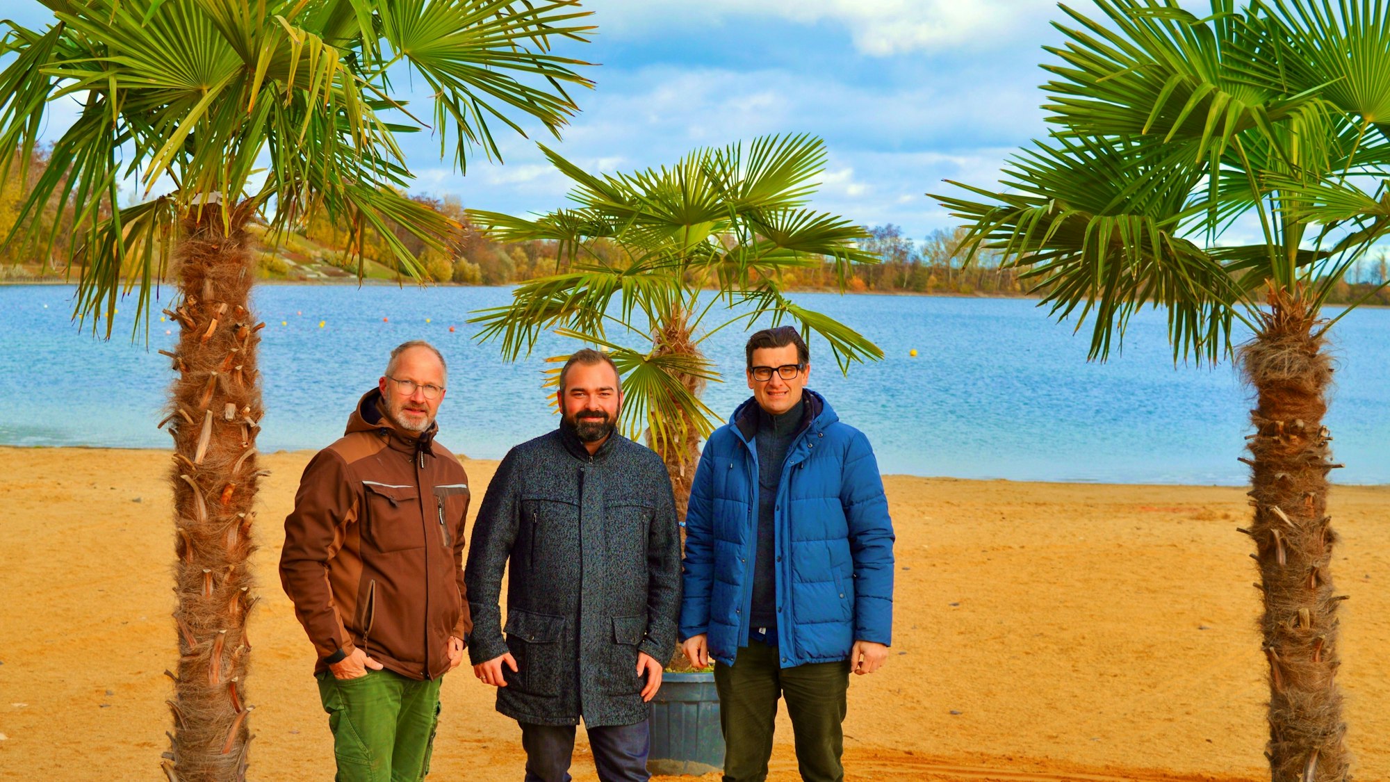 Drei Männer stehen unter Palmen im Seepark Zülpich.