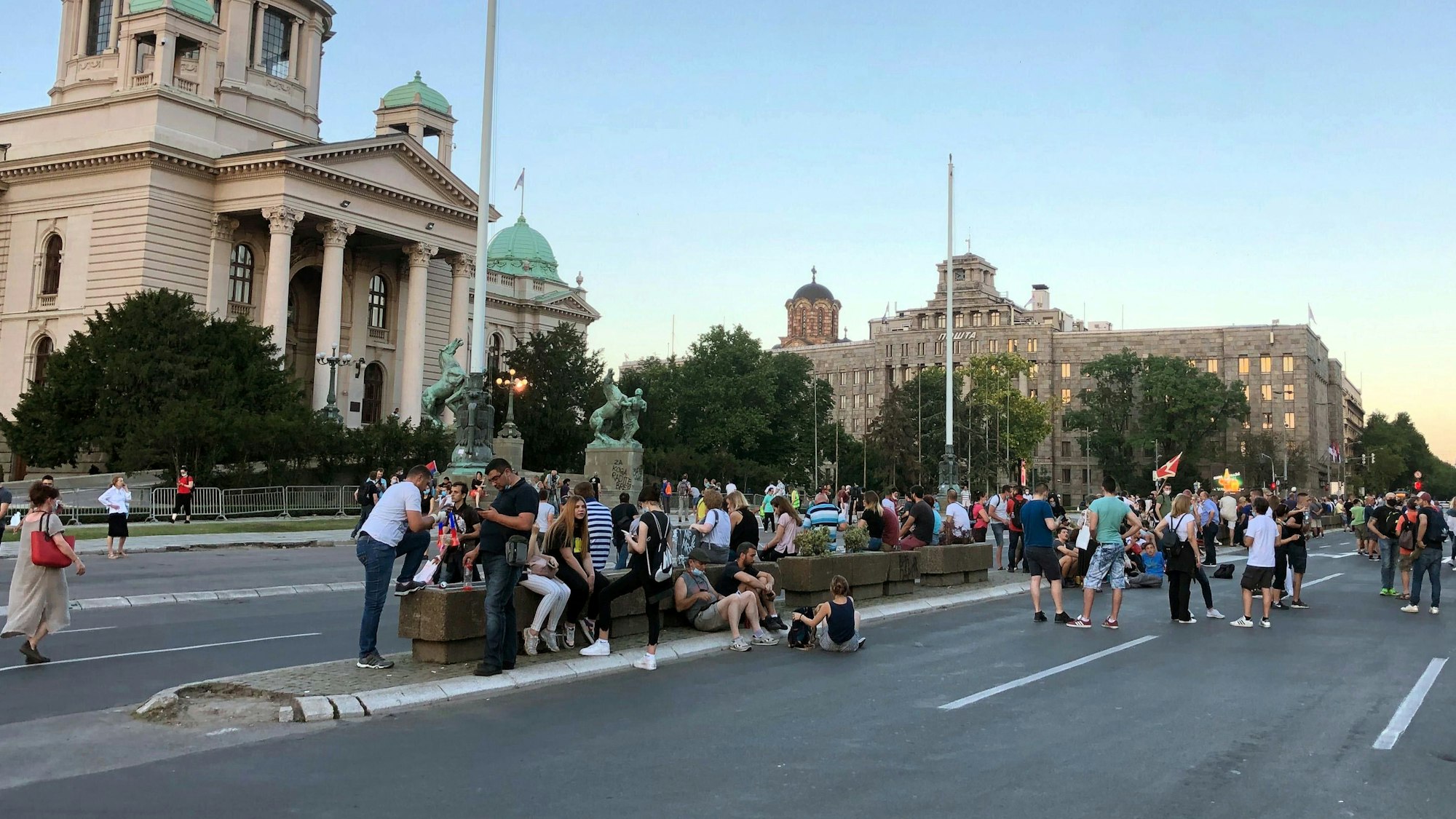 Menschen stehen und sitzen auf der Straße vor dem Parlament und dem Verfassungsgericht in Belgrad.