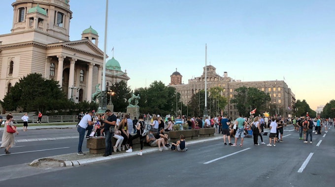 Menschen stehen und sitzen auf der Straße vor dem Parlament und dem Verfassungsgericht in Belgrad.