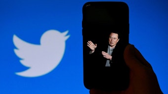 Ein Handy zeigt den Milliardär Elon Musk, der gegen das Twitter-Logo im Hintergrund gehalten wird