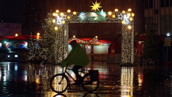 Ein Radfahrer fährt am frühen Morgen bei Schneeregen am Eingang des Weihnachtsmarkts am Dom vorbei.