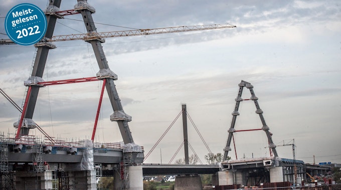 Die zwei neuen Pylone der Leverkusener Brücke sind im Vordergrund zu sehen. Es ist eine große Baustelle. Im Hintergrund ragt der alte Pylon in den leicht bedeckten Himmel.&nbsp;