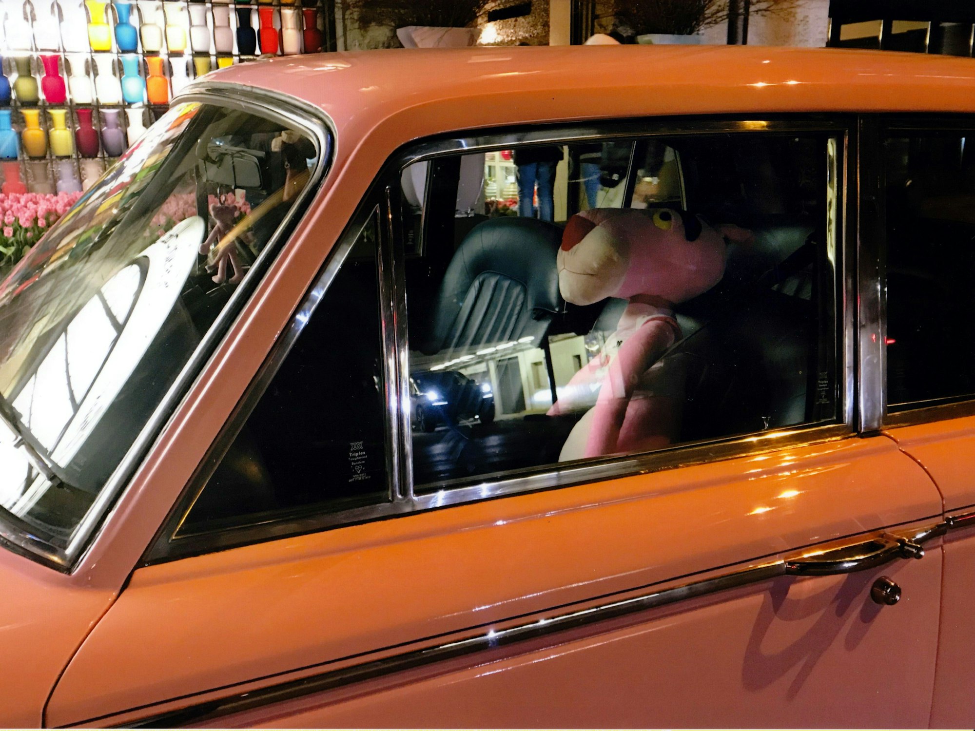 Eine Stofffigur von Paulchen Panther sitzt hinter dem Steuer eines stehenden, orangenen Autos.