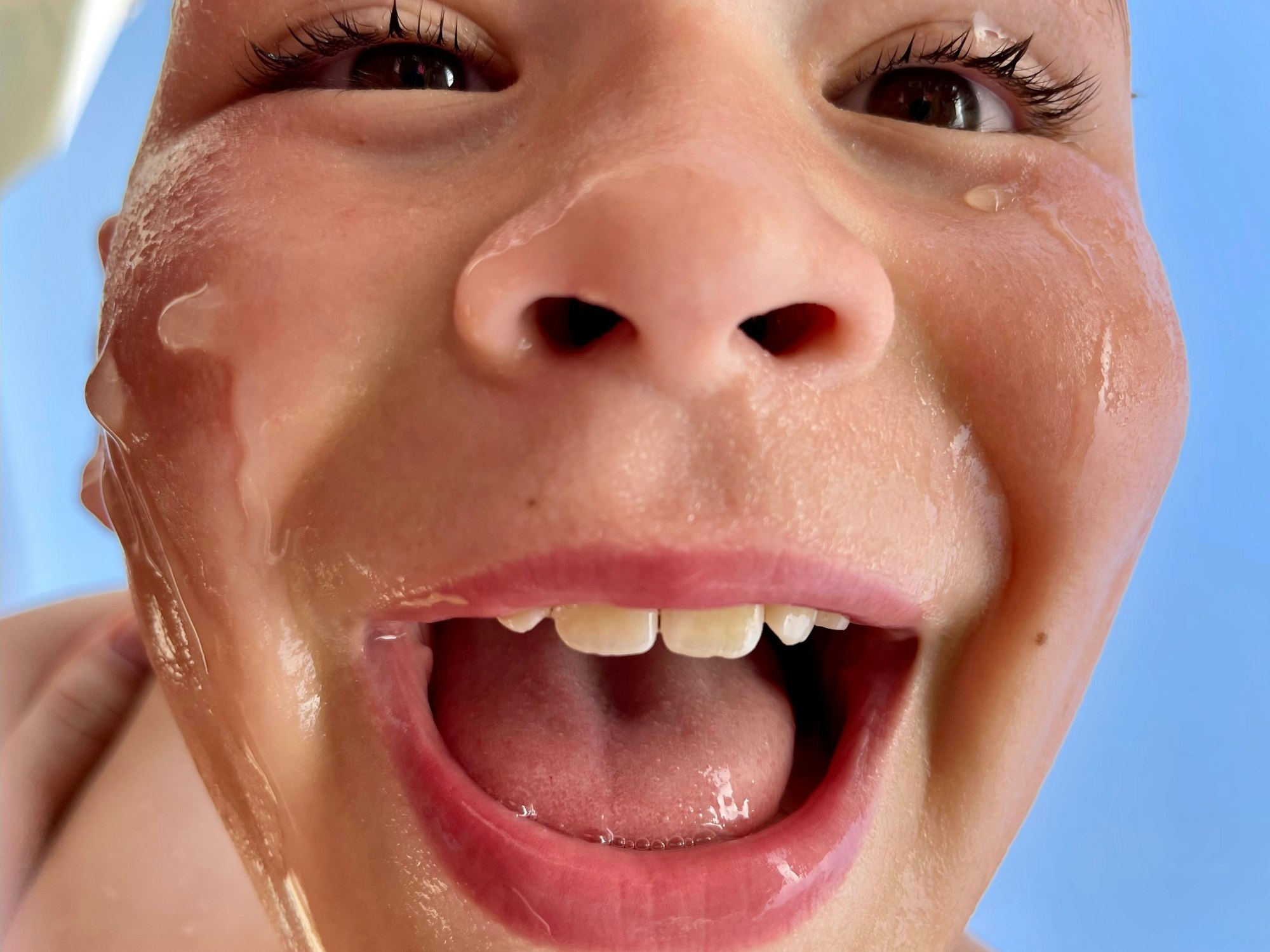 Eine ganz nahe Aufnahme eines Jungen, der mit Wasser im Gesicht in die Kamera strahlt.