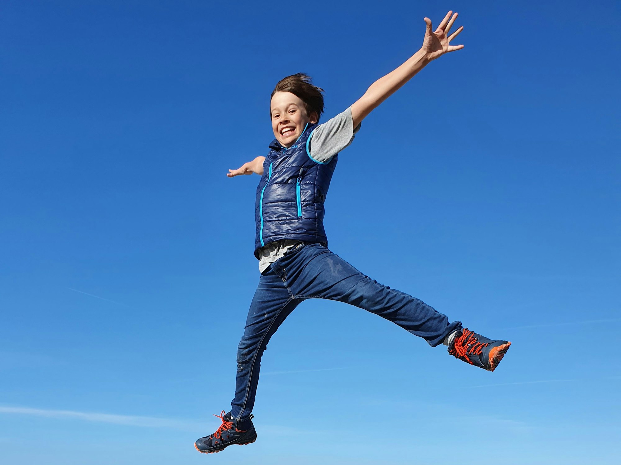 Ein Junge springt, alle Viere von sich gestreckt, an einem Strand auf und ab vor blauem Himmel.