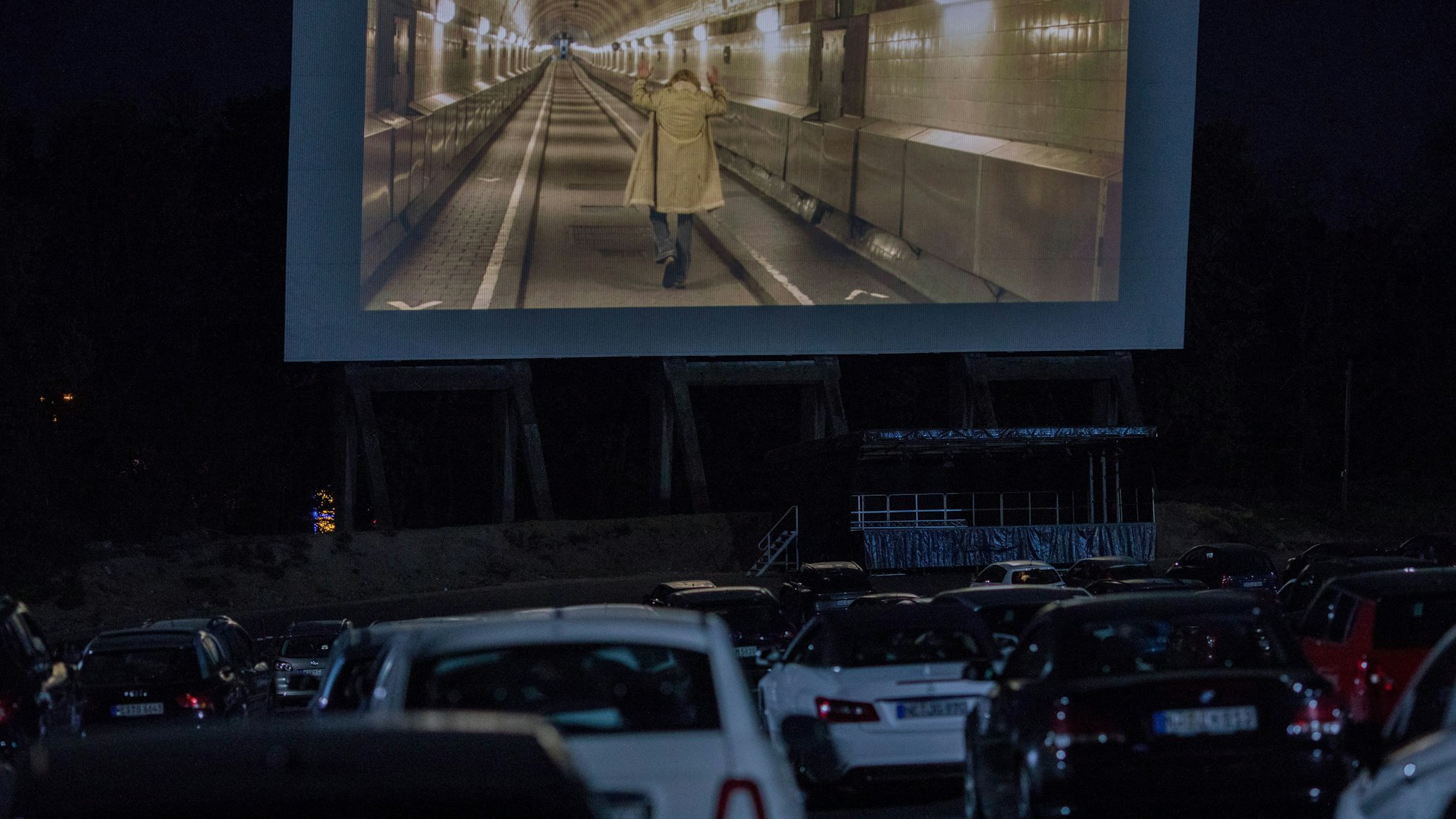 Viele Autos stehen vor einer großen Leinwand im Autokino in Köln-Porz. Auf der Leinwand läuft ein Film.