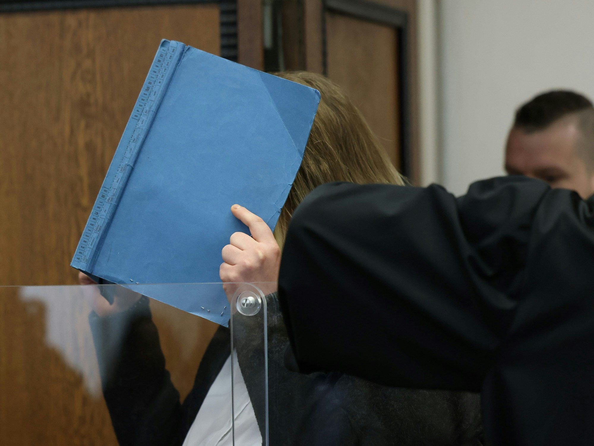 Die Angeklagte deckt ihr Gesicht mit einem blauen Ordner ab, als sie in den Gerichtssaal im Landgericht geführt wird.