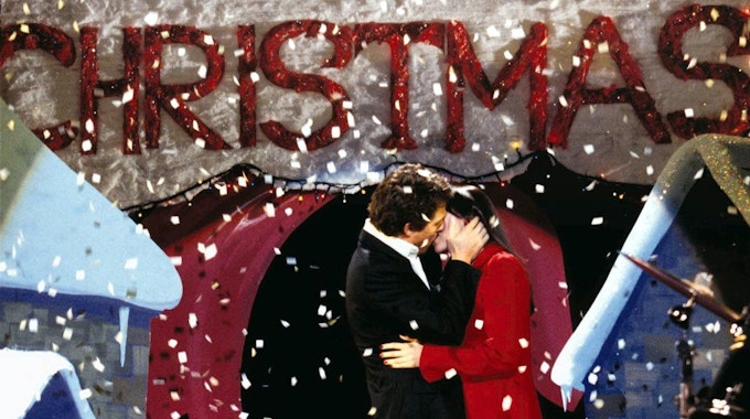 Der englische Premierminister (gespielt von Hugh Grant) küsst seine Angestellte Natalie (gespielt von Martine McCutcheon) auf einer Bühne. Von oben rieselt weißes Konfetti auf die beiden herab.