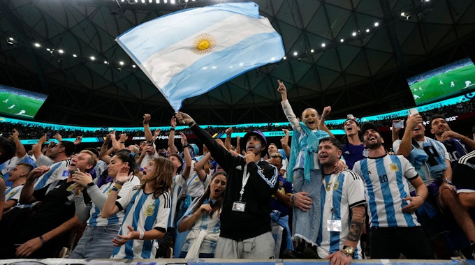 Argentinien-Fans singen bei einem WM-Spiel lautstark und schwenken eine argentinische Flagge.