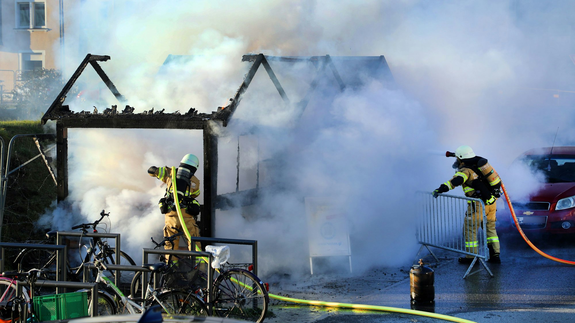 Zwei Feuerwehrleute löschen ein brennendes Holzhäuschen. Große Rauchwolken steigen auf.