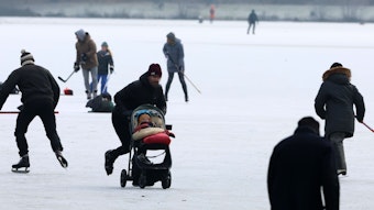 Menschen mit Schlittschuhen sind auf dem zugefrorenen Decksteiner Weiher. Ein Mann schiebt einen Kinderwagen übers Eis.