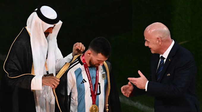 Der katarische Emir Emir Tamim bin Hamad Al Than zieht Lionel Messi bei der WM-Siegerehrung einen goldverzierten Umhang über. Fifa-Präsident Gianni Infantino steht daneben.