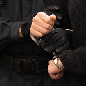 Ein Polizist hält Hände von Gefangenen in Handschellen