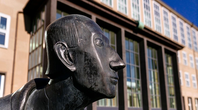 Im Vordergrund der Kopf der Statue von Albertus Magnus, im Hintergrund sieht man das Hauptgebäude der Universität zu Köln.