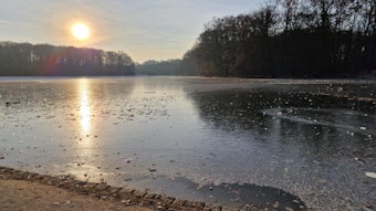 Der Adenauer Weiher in Köln beim Sonnenaufgang, das Gewässer ist zugefroren.