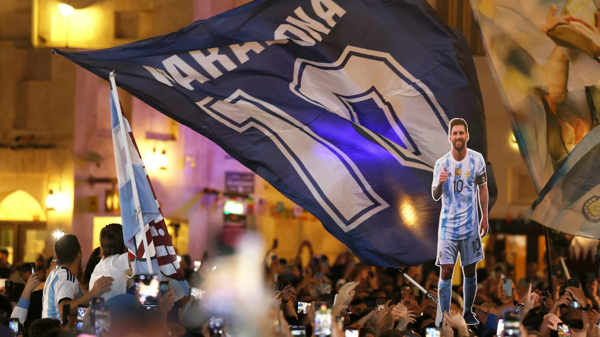 Fans der argentinischen Nationalmannschaft haben sich am Souk Waqif in Doha versammelt. Eine riesige Maradona-Flagge mit der Zehn des Superstars weht, davor ist eine Pappfigur des aktuellen Kapitäns der Argentinier zu sehen, Lionel Messi.