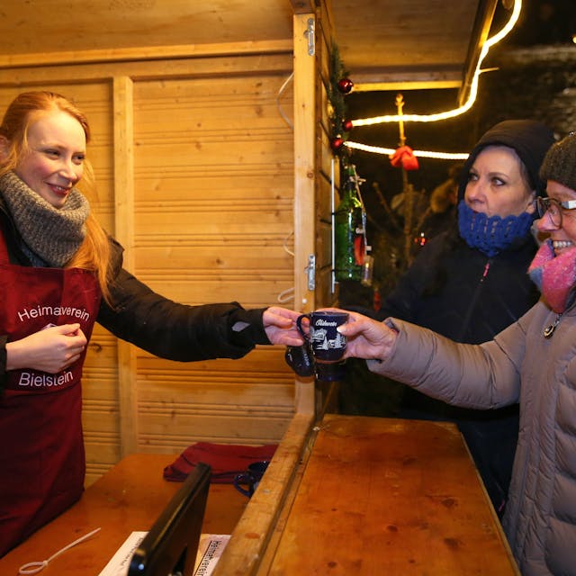Unsere Autorin Lilian Kraft (l.) reicht eine Tasse Glühwein über den Tresen. Sie half am Samstag auf dem Bielsteiner Weihnachtsmarkt in der Glühweinbude des Heimatvereins mit und berichtet hier.&nbsp;