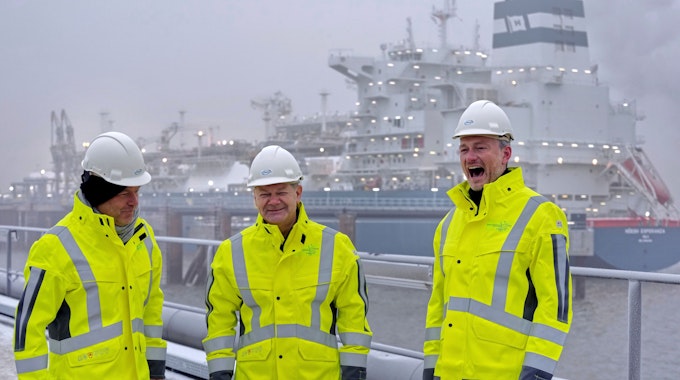 Ribert Habec, Olaf Scholz und Christian Lindner stehen bei der Eröffnung des ersten deutschen LNG-Terminals in Wilhelmshaven vor dem Spezialschiff „Höegh Esperanza“.