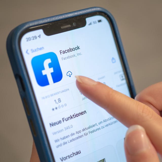 Das Facebook-Logo ist auf einem Handy zu sehen. Eine Frauenhand tippt auf das Download-Icon neben dem Logo.