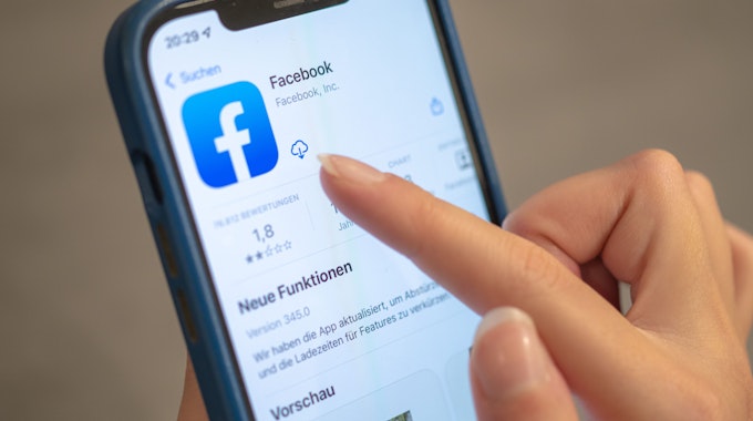 Das Facebook-Logo ist auf einem Handy zu sehen. Eine Frauenhand tippt auf das Download-Icon neben dem Logo.