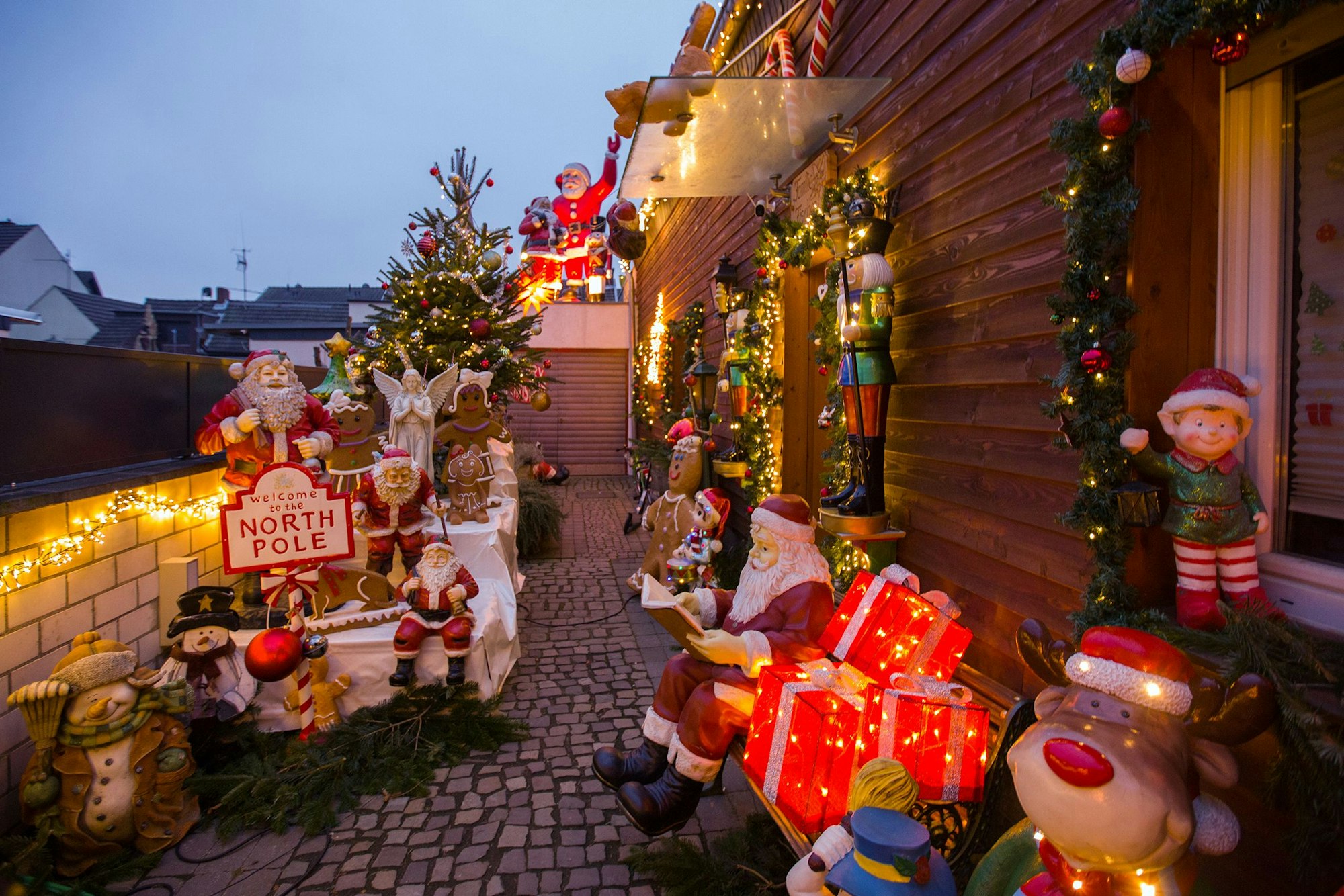 Beleuchtetes Weihnachtshaus von Familie Fischer in Köln-Worringen. Vor dem Haus stehen zahlreiche Weihnachtsfiguren darunter ein Weihnachtsmann, ein Rentier und Nussknacker.
