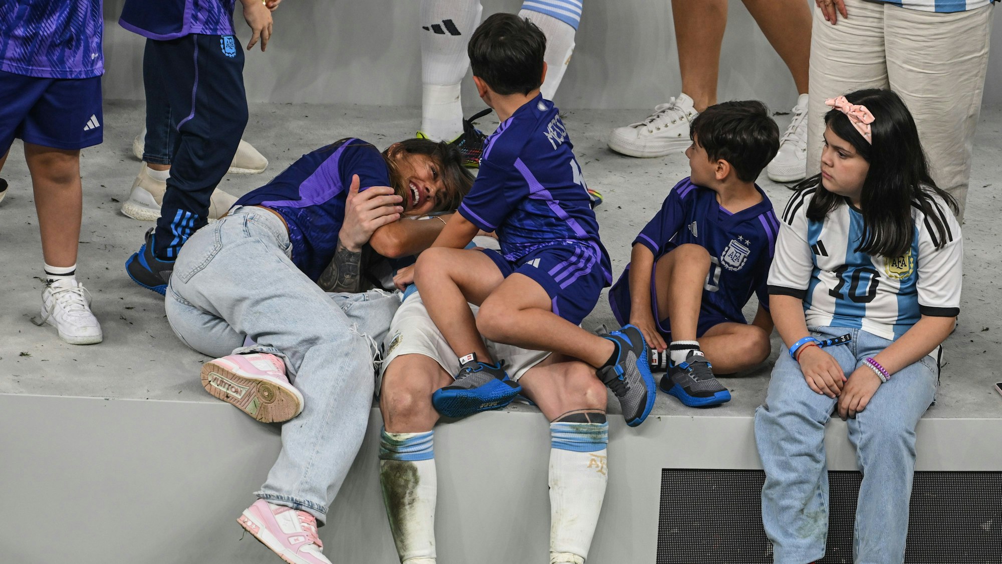 Lionel Messi liegt auf dem Boden, neben ihm Frau Antonella, auf seinem Schoss sein Sohn.