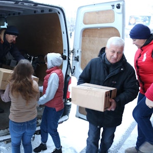 Männer, Frauen und Kinder helfen beim Entladen eines weißen Transporters, sie reichen sich Kartons an.