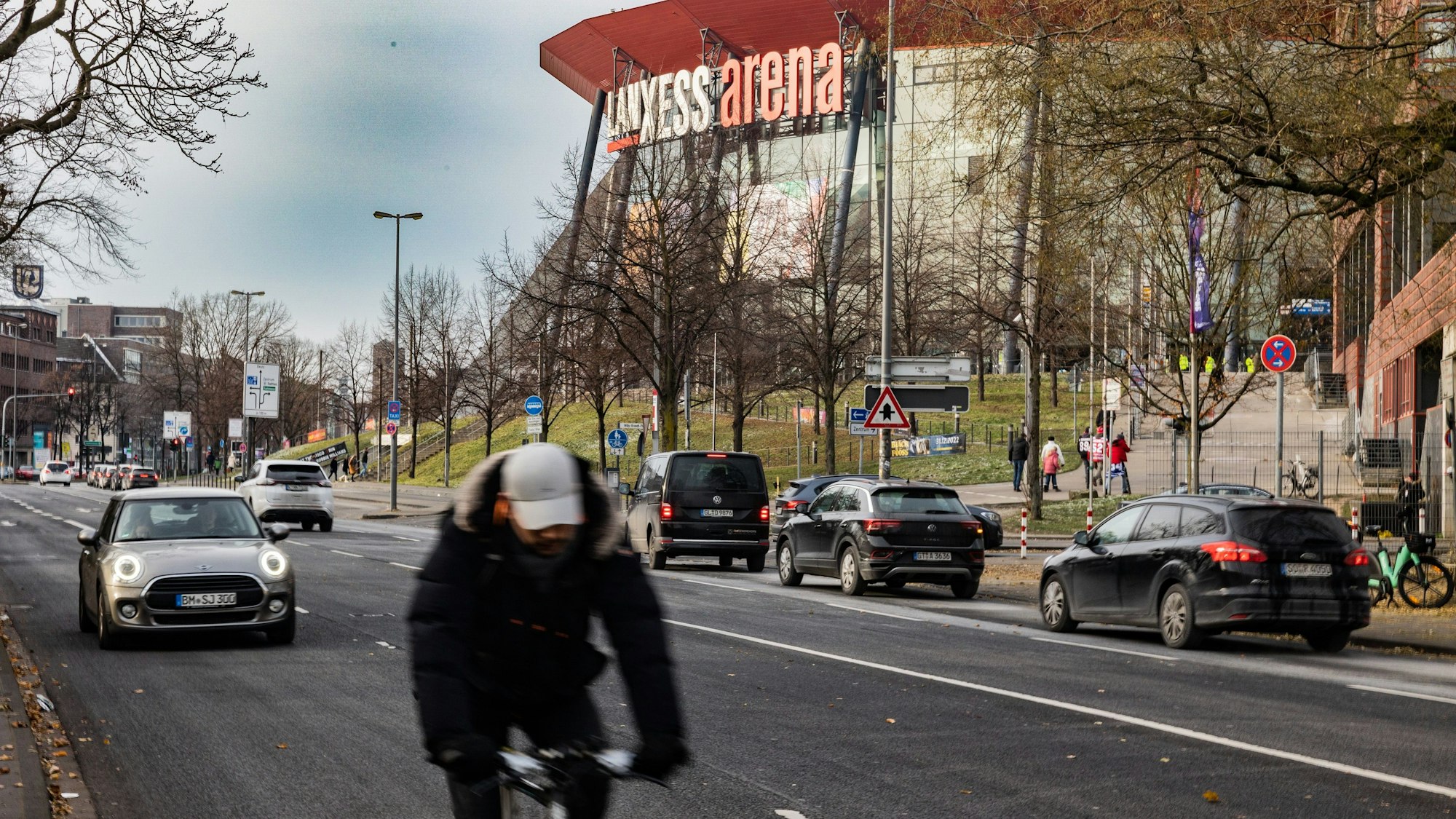 Ein Radfahrer fährt auf der Gummersbacher Straße an der Lanxess-Arena im Kölner Stadtteil Deutz vorbei. Im Hintergrund sind fünf Autos zu sehen.