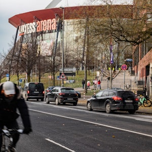 Ein Radfahrer fährt auf der Gummersbacher Straße an der Lanxess-Arena im Kölner Stadtteil Deutz vorbei. Im Hintergrund sind fünf Autos zu sehen.